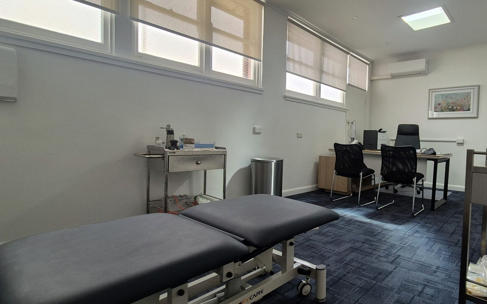 A consulting room with a treatment bed, a desk and chairs